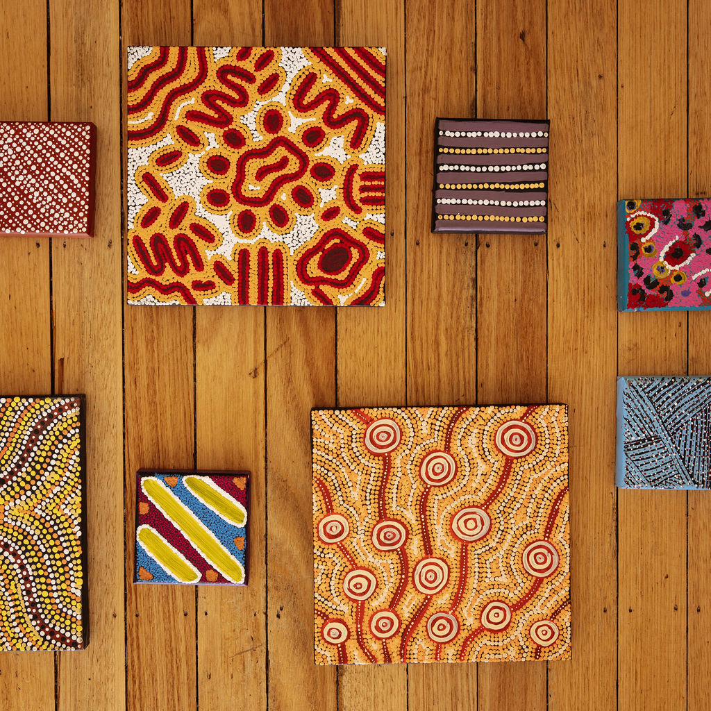 First Nations canvas artworks arranged on a wooden floor. 