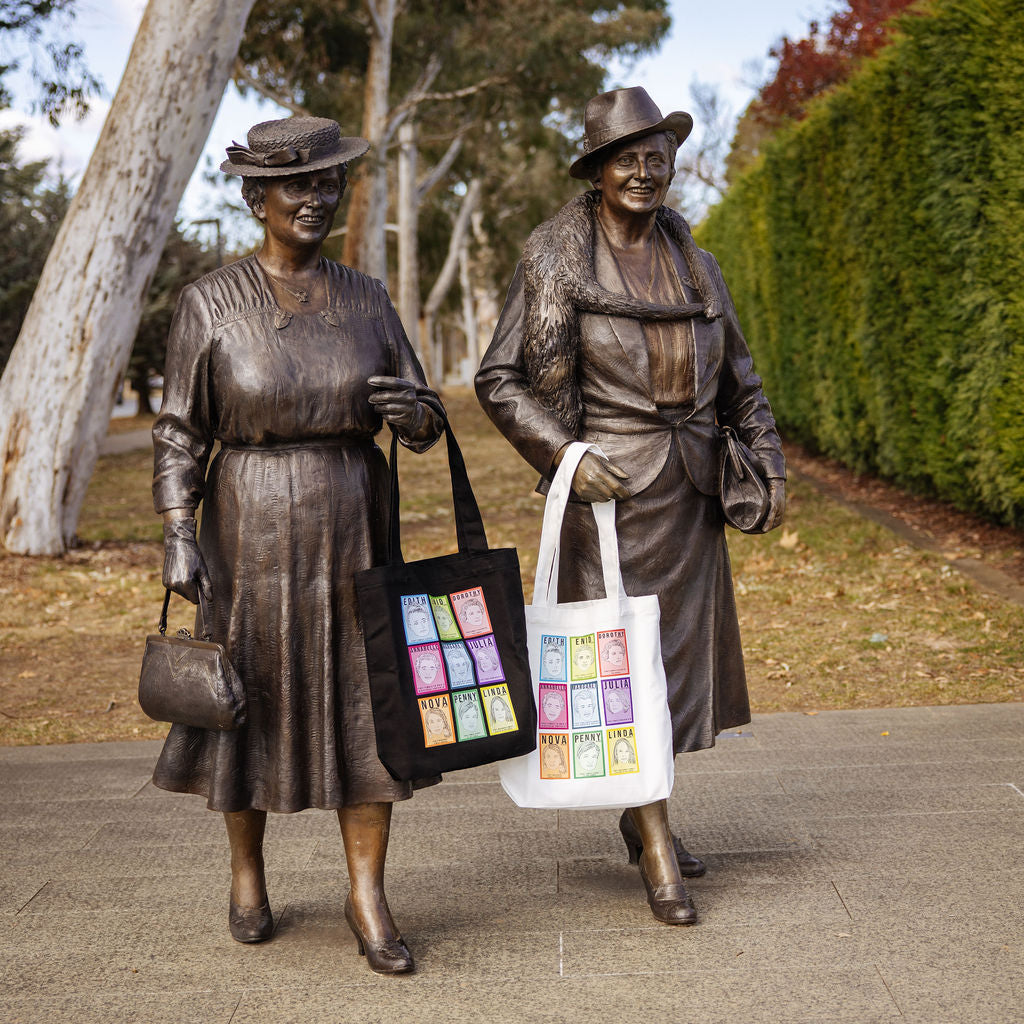 Two statues of women politicians carry tote bags featuring women in politics. 