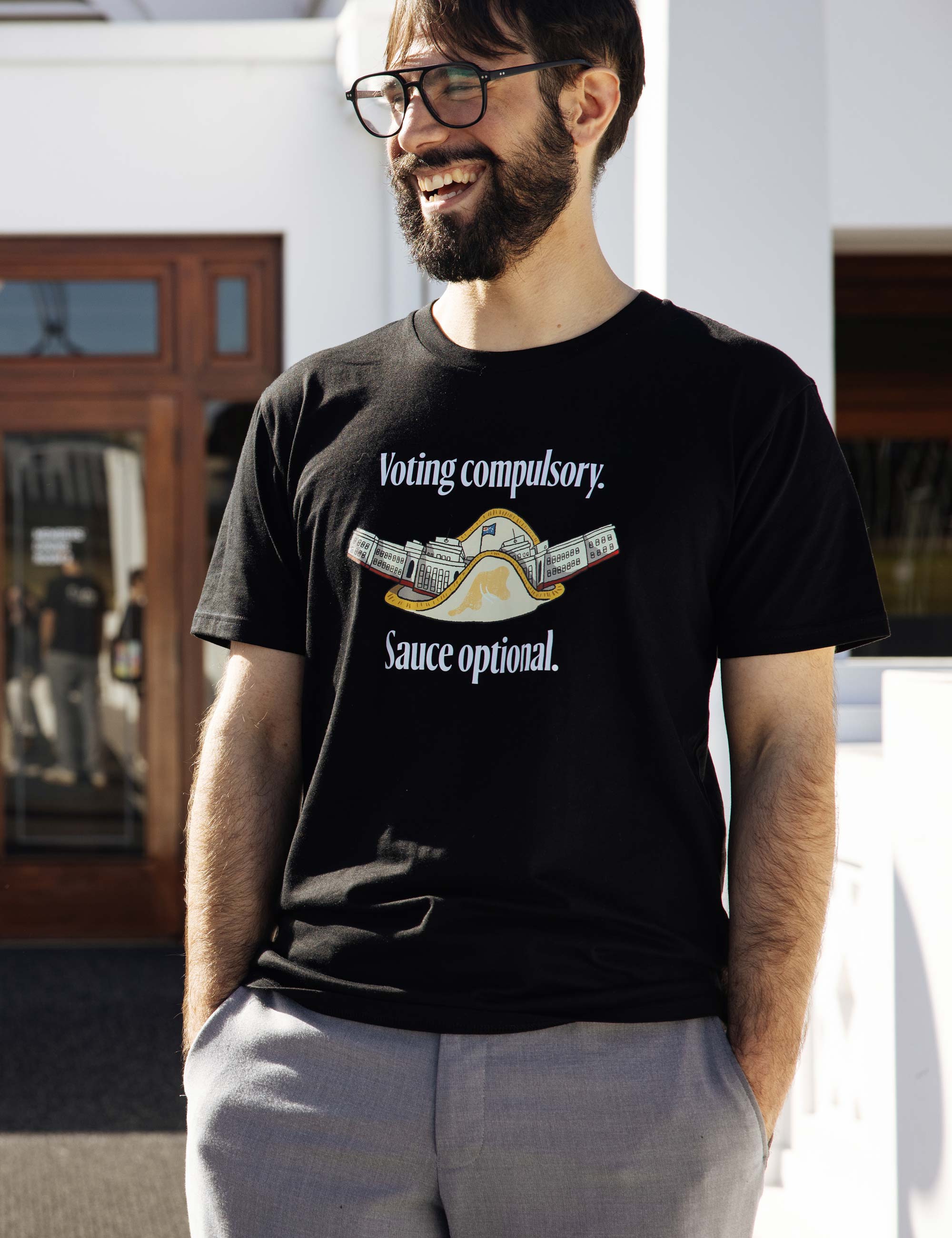 A person wearing a black t-shirt with the words 'Voting compulsory. Sauce Optional' around a sausage sandwich design. 